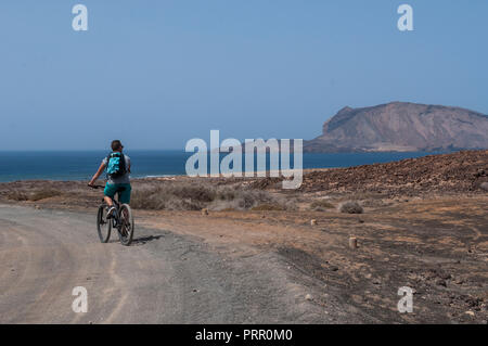 Lanzarote, Canary Islands: boy biking on the dirt road to the beach Playa de Las Conchas in the north of La Graciosa, main archipelago island Chinijo Stock Photo