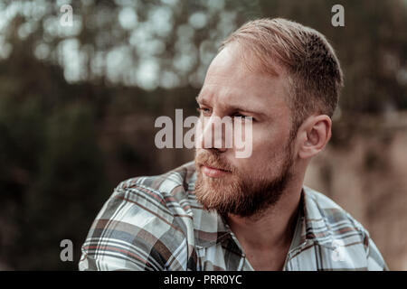 Close up of handsome bearded blonde-haired man feeling rather serious