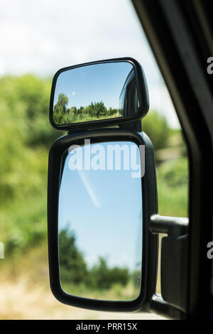 Truck dashboard with driver's hand on the steering wheel and side rear-view mirror against night sky with sunset Stock Photo