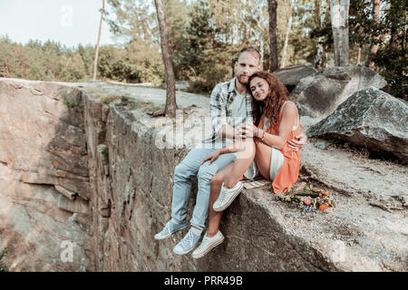 Cute young loving couple relaxing while sitting on the rock near lake Stock Photo