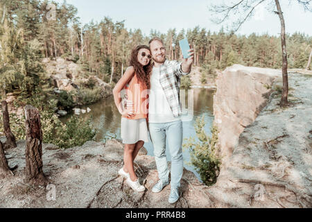 Beaming curly woman posing for photo with her husband while resting in nature Stock Photo