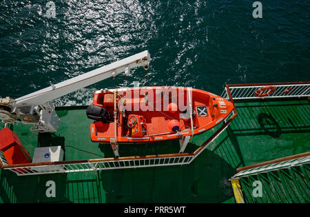 Small orange boat with an outboard engine attached to a swinging gantry on a ferry. For man overboard.