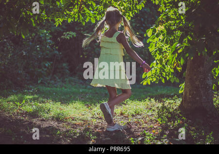 beautiful caucasian girl with long blond hair in yellow dress dancing under the tree in summer time Stock Photo