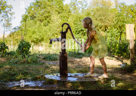 little lovely girl pumping water well to water growing vegetables in the countryside Stock Photo