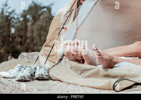 Close up of barefooted backpackers lying in tent standing near their sneakers Stock Photo