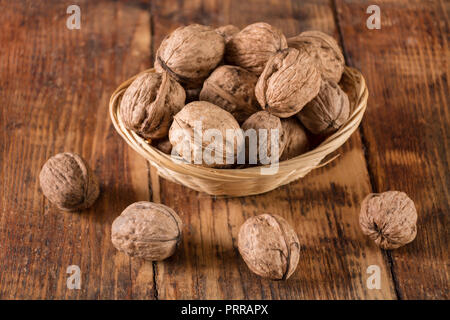 Walnuts in retro bowl and spilled on wooden desk. Autumn food concept. Close up, selective focus Stock Photo