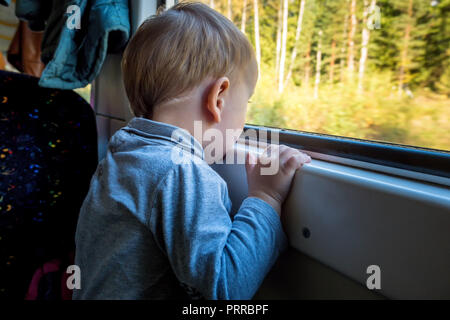 Beautiful toddler boy looking out train window outside, while it moving. Going on vacations and traveling by railway in winter Stock Photo