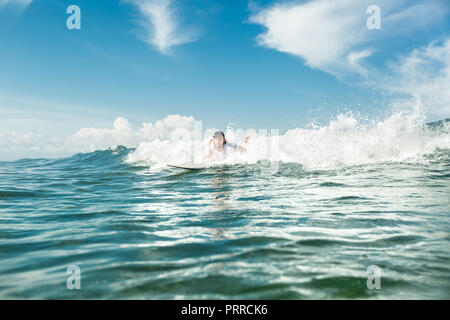 male surfer swimming on surfing board in ocean at Nusa Dua Beach, Bali, Indonesia Stock Photo