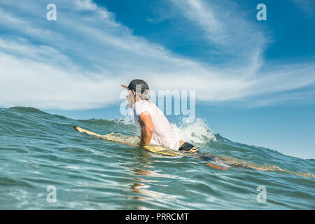 side view of male surfer swimming on surfing board in ocean at Nusa Dua Beach, Bali, Indonesia Stock Photo