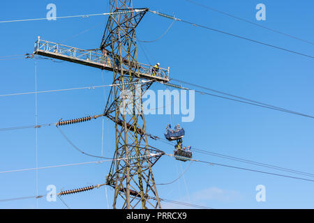 Workers replacing high voltage electricity cable on a pylon using platforms and baskets suspended from the pylon Stock Photo