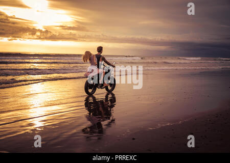 rear view of boyfriend and girlfriend riding motorbike on ocean beach during sunrise Stock Photo