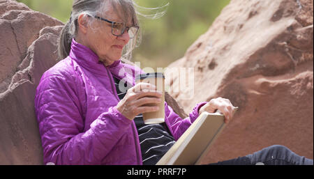 Mature outdoors enthusiast smiling and reading book in nature seated on