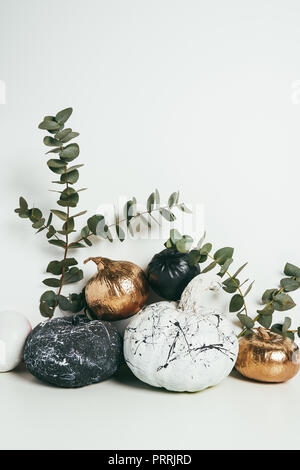 still life with golden, black and white pumpkins with paint splatters and eucalyptus on white Stock Photo