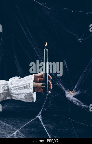 cropped view of scary woman holding black candle in darkness with spider web Stock Photo