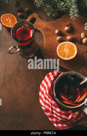 homemade hot mulled wine in glass cup and saucepan with fresh oranges and spices on wooden background Stock Photo