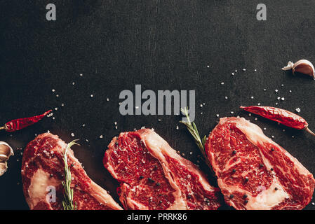 elevated view of raw meat steaks and spices on surface in kitchen Stock Photo