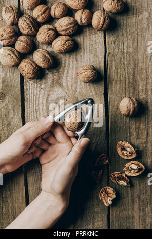 partial top view of of person cracking walnut with nutcracker above wooden table Stock Photo