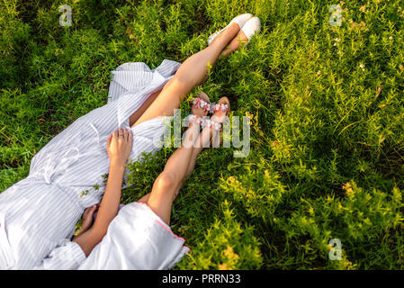 cropped shot of mother and daughter in white dresses lying on green grass Stock Photo