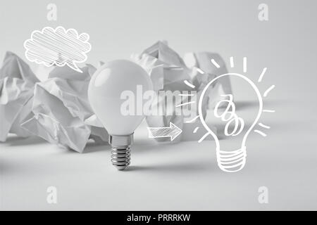 white light bulb with drawn light bulb sign on background with crumpled papers Stock Photo