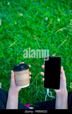 girl viewing the smart teleofnu sitting in the grass field and drinking coffee Stock Photo