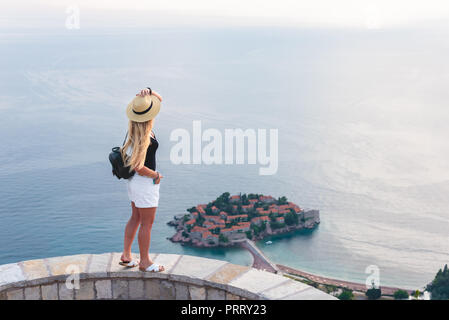 woman standing and looking at saint stephen island in Adriatic sea, Budva, Montenegro Stock Photo