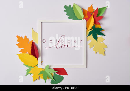 flat lay with handcrafted paper leaves and empty frame with "october love" inspiration on white tabletop Stock Photo