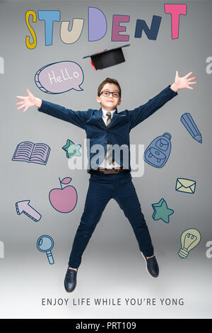 schoolboy in graduation cap jumping, isolated on grey with educational icons and "student - enjoy life while youre yong" lettering Stock Photo