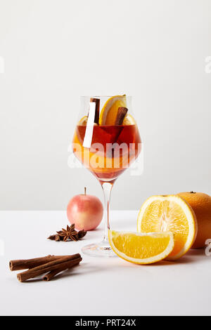 close up view of mulled wine in glass and ingredients arranged around on white tabletop on grey backdrop Stock Photo