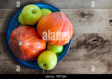 pumpkins and apples in ceramic bowl on rustic wooden kitchen table Stock Photo