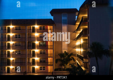 Night time establishing shot looking at generic apartment condo building balcony entrances on multiple floors. Porch lights illunimate dark setting Stock Photo