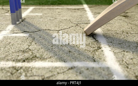 A tip of a cricket bat sliding over the crease on a cracked grass pitch background - 3D render Stock Photo