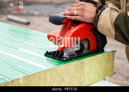 A young man welder in a working overall and working gloves grinds a sandwich panels  with a angle  grinder in the constraction side Stock Photo