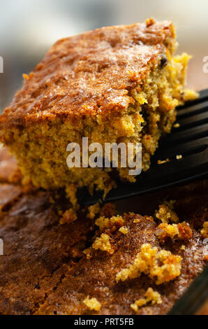 A slice of carrot cake, lifted out of baking dish with remainder and crumbs below. Close up side corner view. Stock Photo