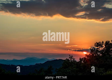 Sun hiding behind clouds during colorful summer sunset near the Stone Mushrooms natural phenomenon in South Bulgaria, near town of Kardzhali Stock Photo