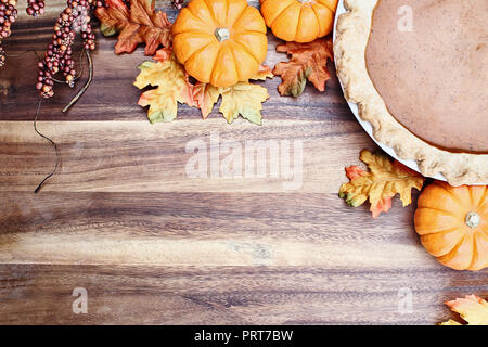 Homemade pumpkin pie in pie plate with little pumpkins, autumn leaves and room for text over rustic wooden background. Image shot from overhead. Stock Photo