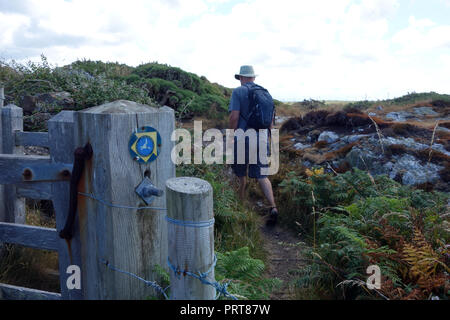 Lone Man Hiker Walking past Wooden Gate & Signpost for the Isle of Anglesey Coastal Path near the Fishing Village of Cemaes, Wales, UK. Stock Photo