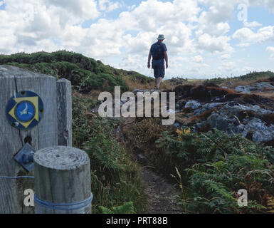 Lone Man Hiker Walking past Wooden Gate & Signpost for the Isle of Anglesey Coastal Path near the Fishing Village of Cemaes, Wales, UK. Stock Photo