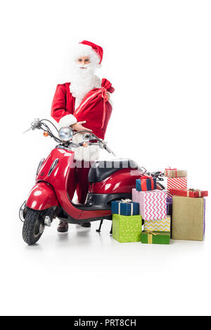 santa claus with christmas sack standing near scooter and pile of gift boxes isolated on white background Stock Photo