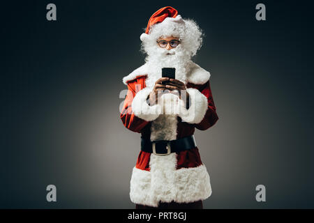happy santa claus in costume using smartphone isolated on grey background Stock Photo