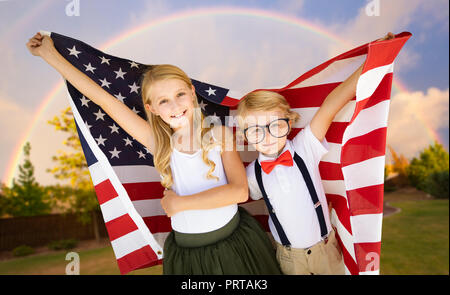 Cute Young Cuacasian Boy and Girl Holding American Flag With Rainbow Behind. Stock Photo