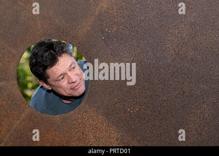 Handsome mature man in the iron plate hole, looking at the camera, facial expressions, screams, smile, amazement, nature background, for advertising Stock Photo