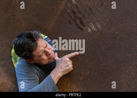 Handsome mature man in the iron plate hole, looking at the camera, facial expressions, screams, smile, amazement, nature background, for advertising Stock Photo