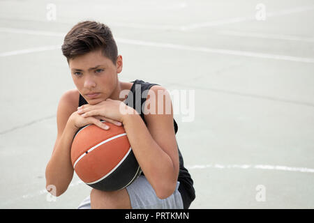 Male teenage basketball player crouching with ball on basketball court, portrait Stock Photo