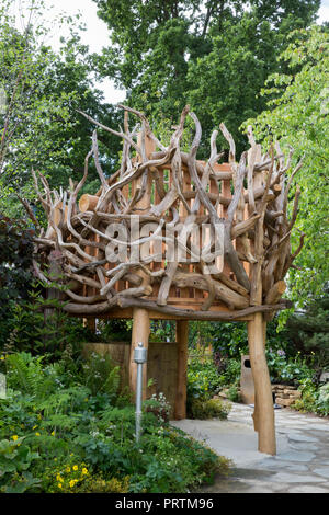 large stone boulder paved slab path leading to wooden nest treehouse made from driftwood, viewing area planted below with Epimediums, ferns, Geraniums Stock Photo