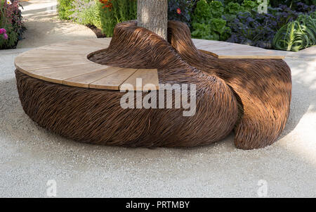 Garden with Woven willow and wooden bench seating under tree, gravel path patio and seating area UK summer Stock Photo