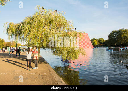 A young couple stand in front of a weeping willow tree next to Christo & Jeanne-Claude's The London Mastaba, on London's Serpentine, London, UK Stock Photo