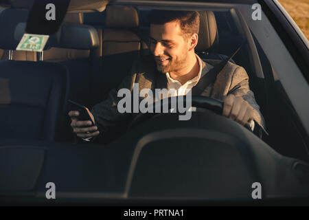 Front view of smiling bussinesman in suit driving his car, using mobile phone Stock Photo