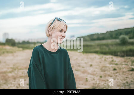 smiling blonde woman with sunglasses on head looking away while standing outdoors Stock Photo