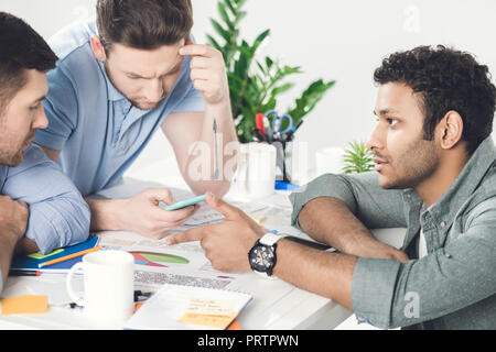 Three young businessmen sitting at table and working on new project together, business teamwork concept Stock Photo