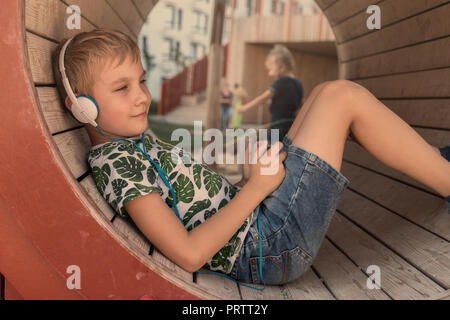Smiling boy with smartphone and headphones listening to music or playing game outdoor Stock Photo